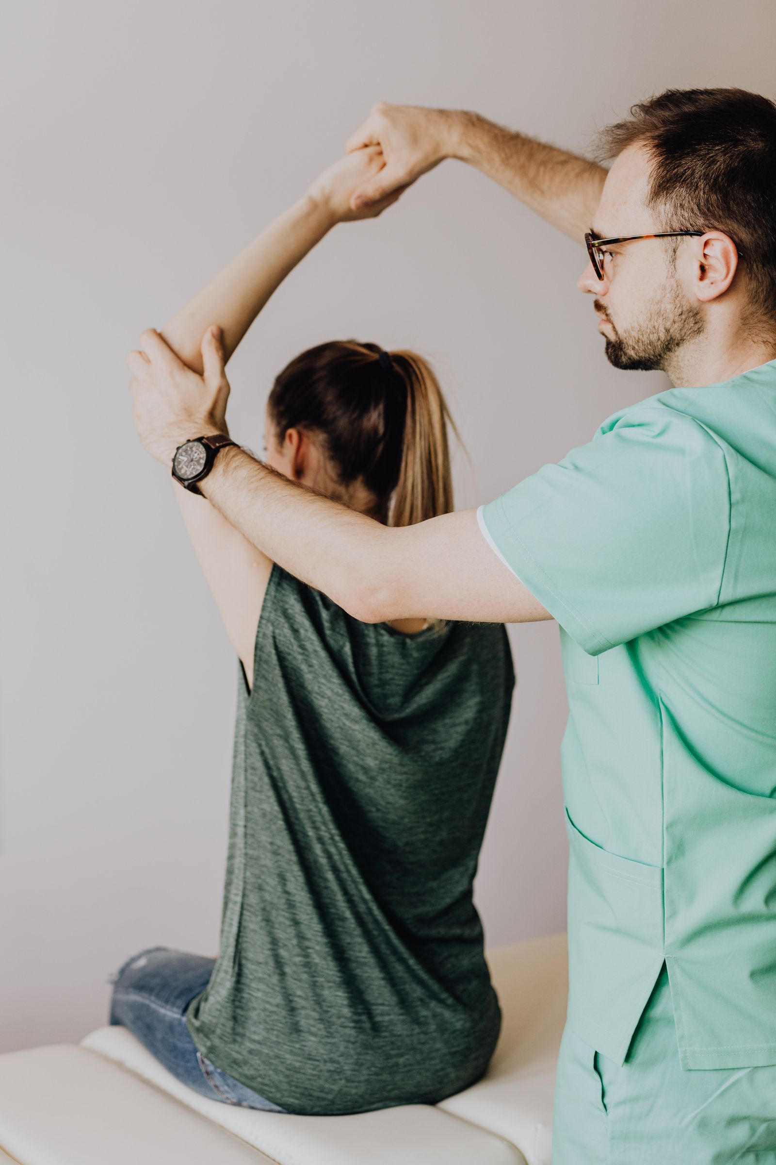 Physiotherapist guiding a patient's arm through an overhead rehabilitation stretch